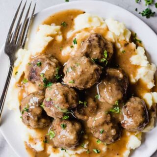 A plate filled with mashed potatoes that are topped with meatballs and gravy.