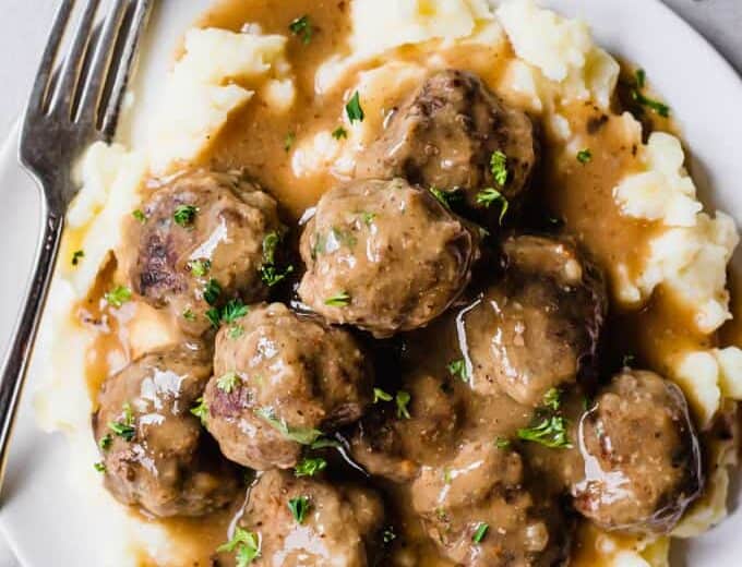 A plate filled with mashed potatoes that are topped with meatballs and gravy.