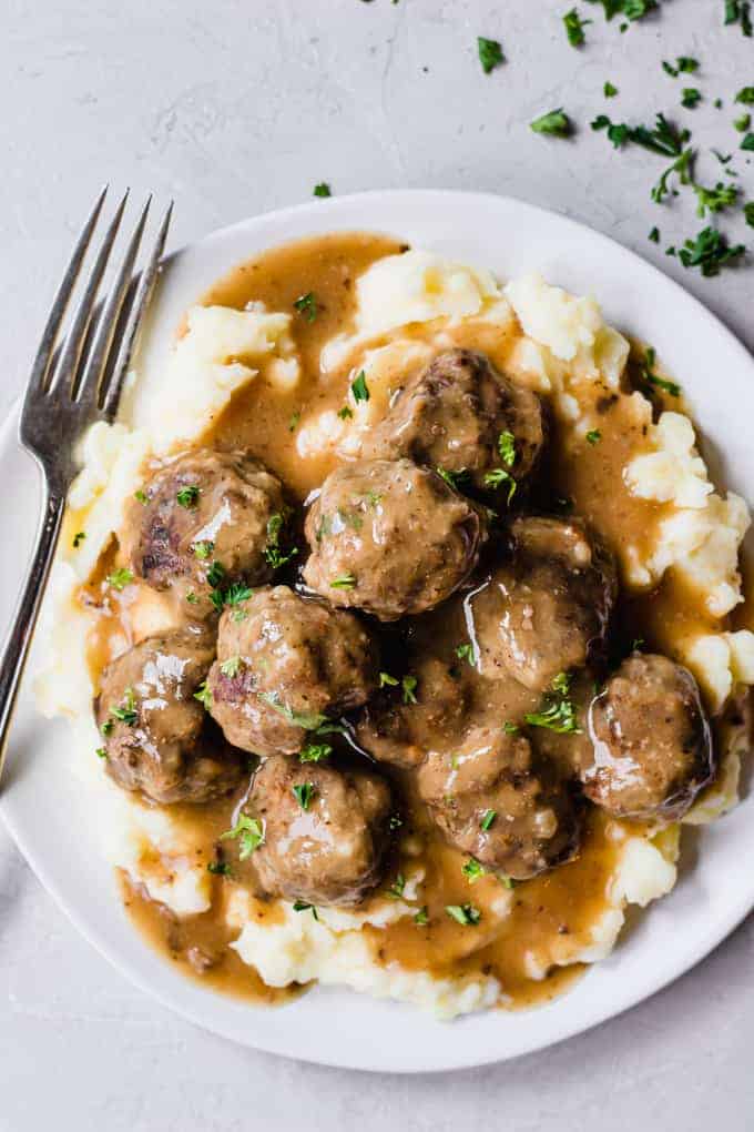 A plate filled with mashed potatoes that are topped with meatballs and gravy.