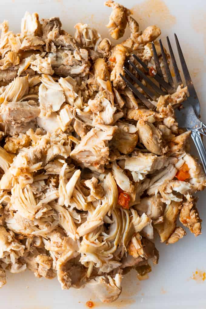 Shredded chicken with two forks ready to add to a pot of tortilla soup.
