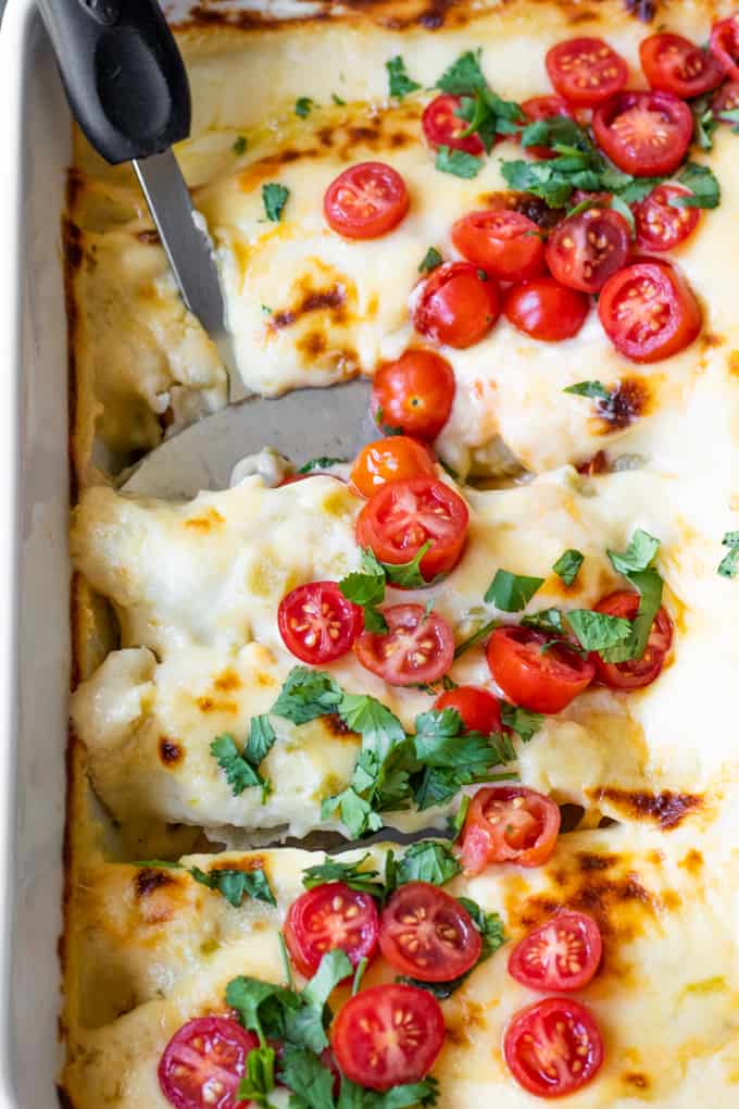 Spatula scooping up cheesy breakfast enchiladas smothered in a queso enchilada sauce.