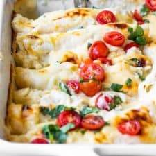Baking dish filled with cheese breakfast enchiladas topped with diced tomatoes and cilantro.