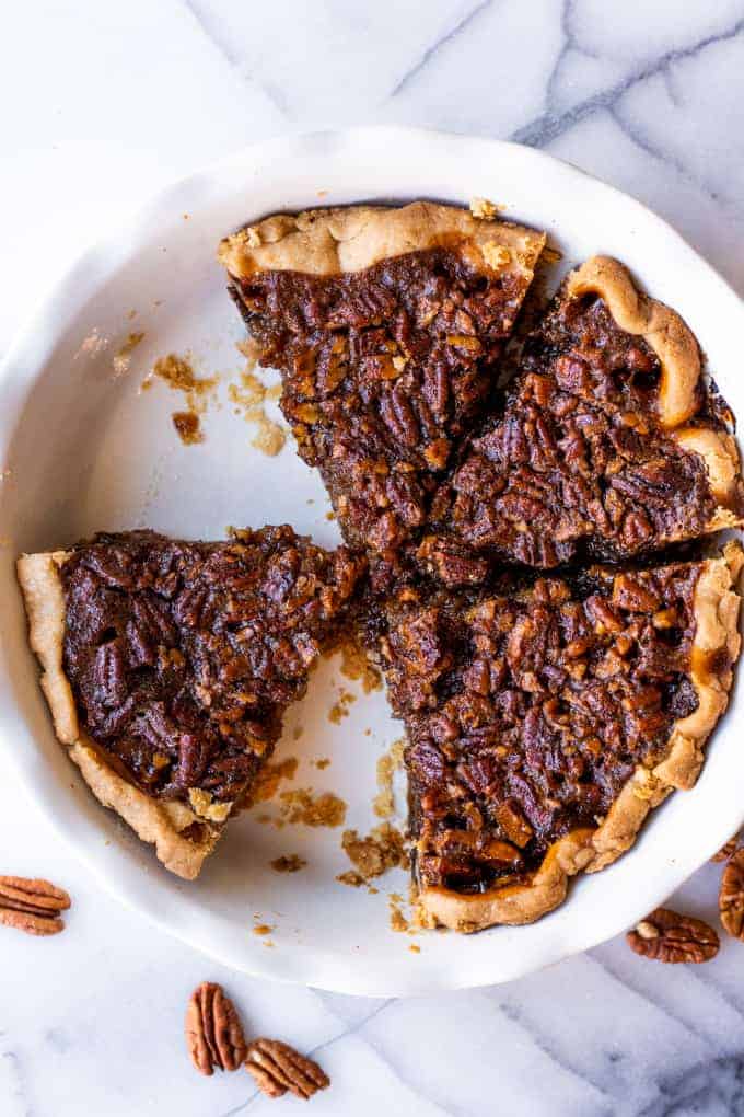 Pie dish with sliced pecan pie, a couple pieces have been removed. 