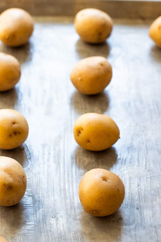 A buttered baking sheet with small gold potatoes set on top.
