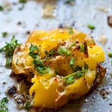 Close of of a baked smashed potato sprinkled with fresh parsley and chives.