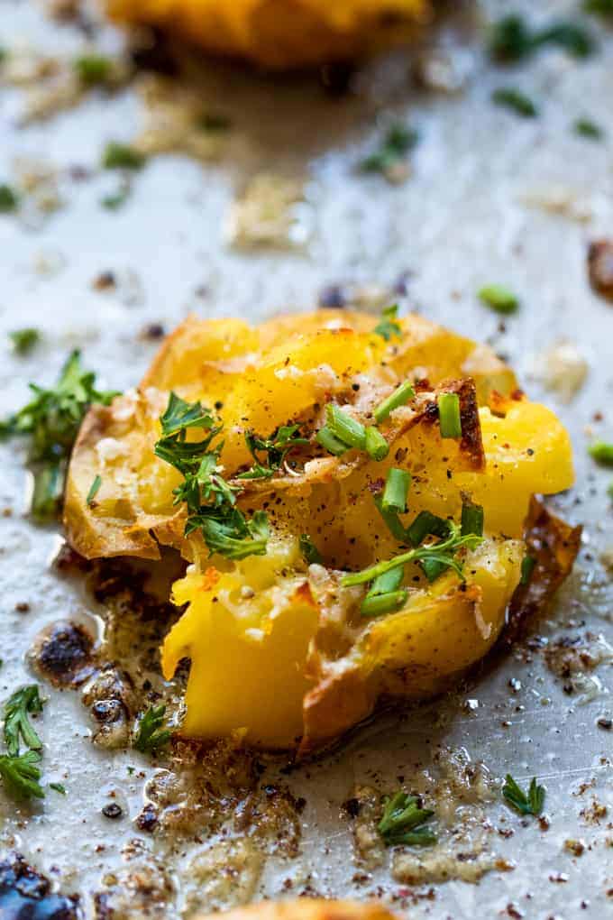 Close of of a baked smashed potato sprinkled with fresh parsley and chives.