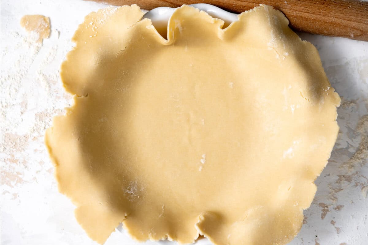 Pie crust laid over a pie dish ready to flute. 