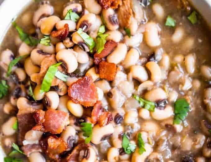 Texas style black eyed peas served in a bowl garnished with crisp bacon and diced cilantro.