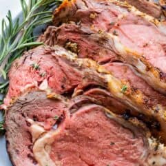 Garlic herb prime rib sliced and laid on a plate garnished with fresh rosemary.