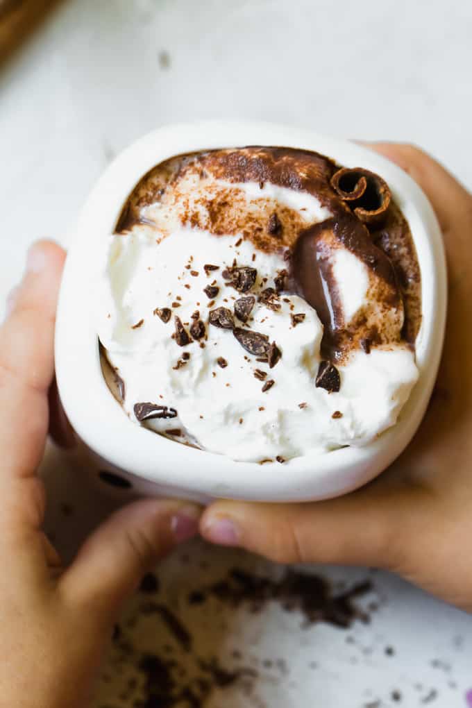 Overhead view of a mug of hot chocolate topped with whipped cream, chocolate shavings and a cinnamon stick.