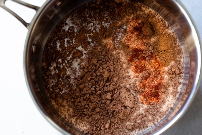 Milk in a saucepan topped with unsweetened cocoa, ground cinnamon, salt, sugar, and chili powder. 