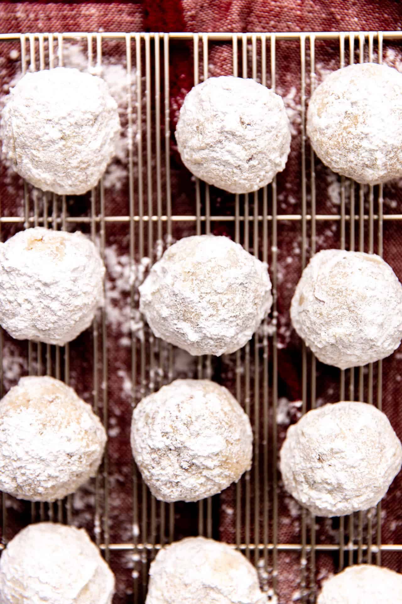 Mexican wedding cookies dipped into powdered sugar and on a wire rack.