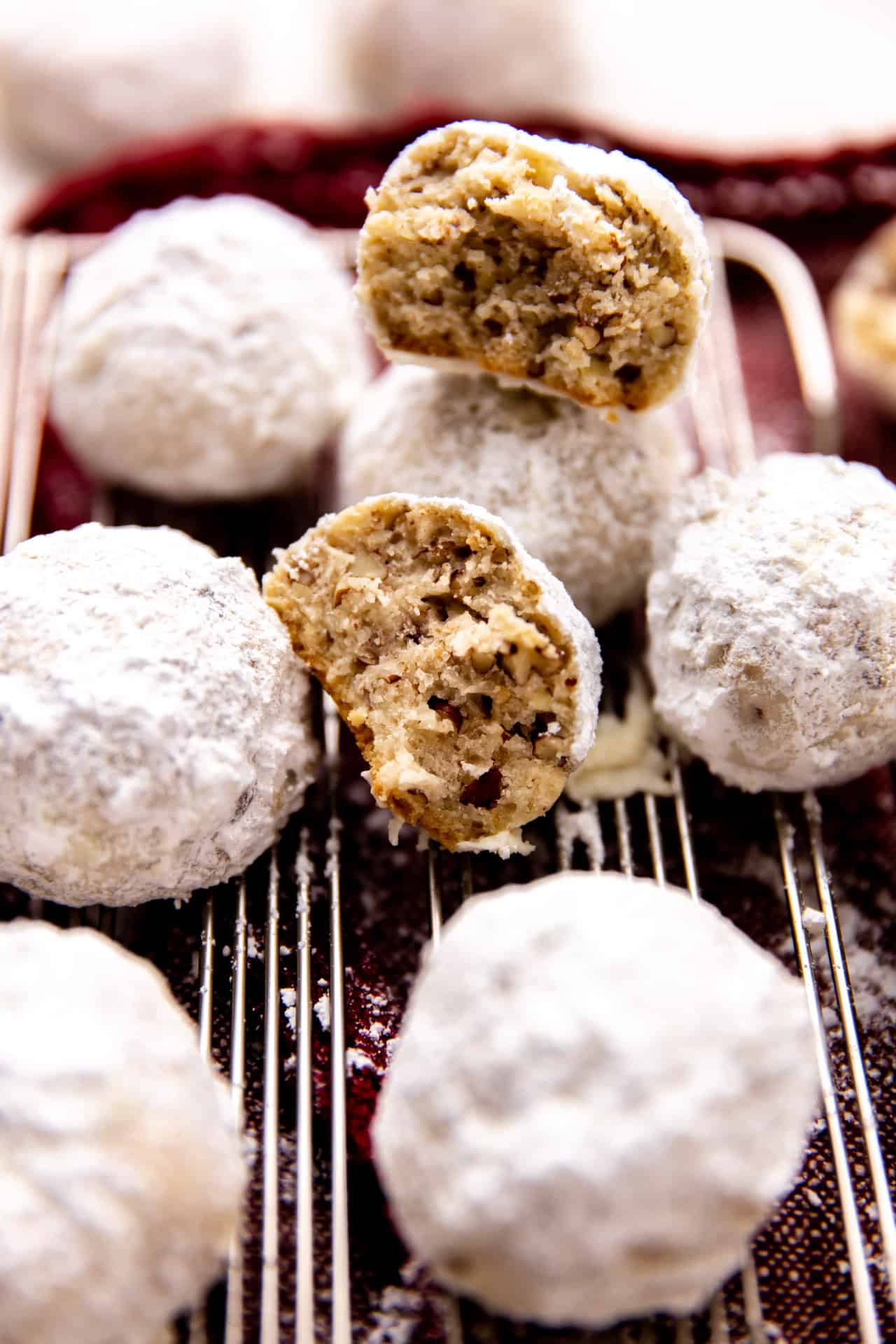 Mexican Wedding cookies on a wire rack, one split in half to see bits of pecans inside. 