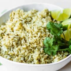 Bowl of green rice topped with cilantro and lime wedges.