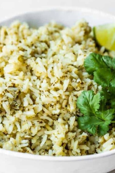 Bowl of green rice topped with cilantro and lime wedges.