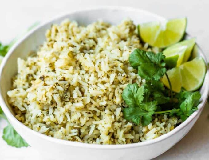 Bowl of green rice topped with cilantro and lime wedges.