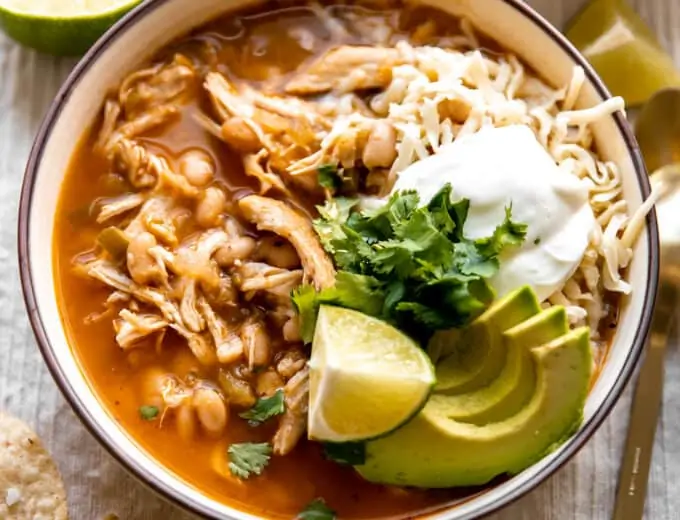 Bowl filled with white chicken chili and topped with cheese, sour cream and avocado.