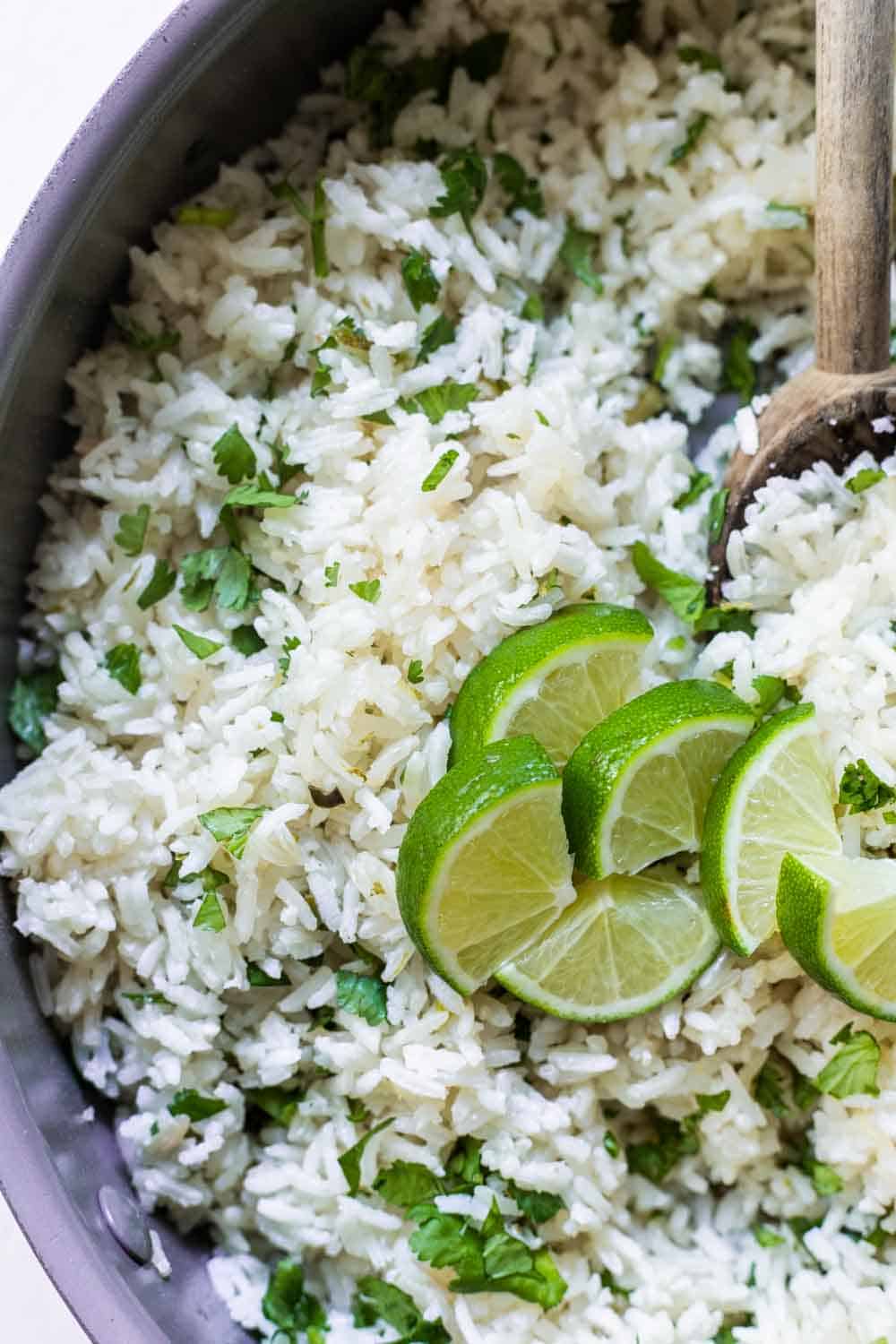 Skillet filled with white rice garnished with fresh cilantro and lime wedges.