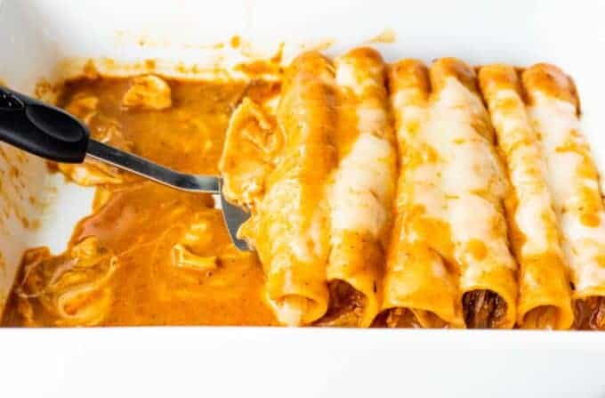 Spatula serving up enchiladas swimming in sauce and melted cheese. 