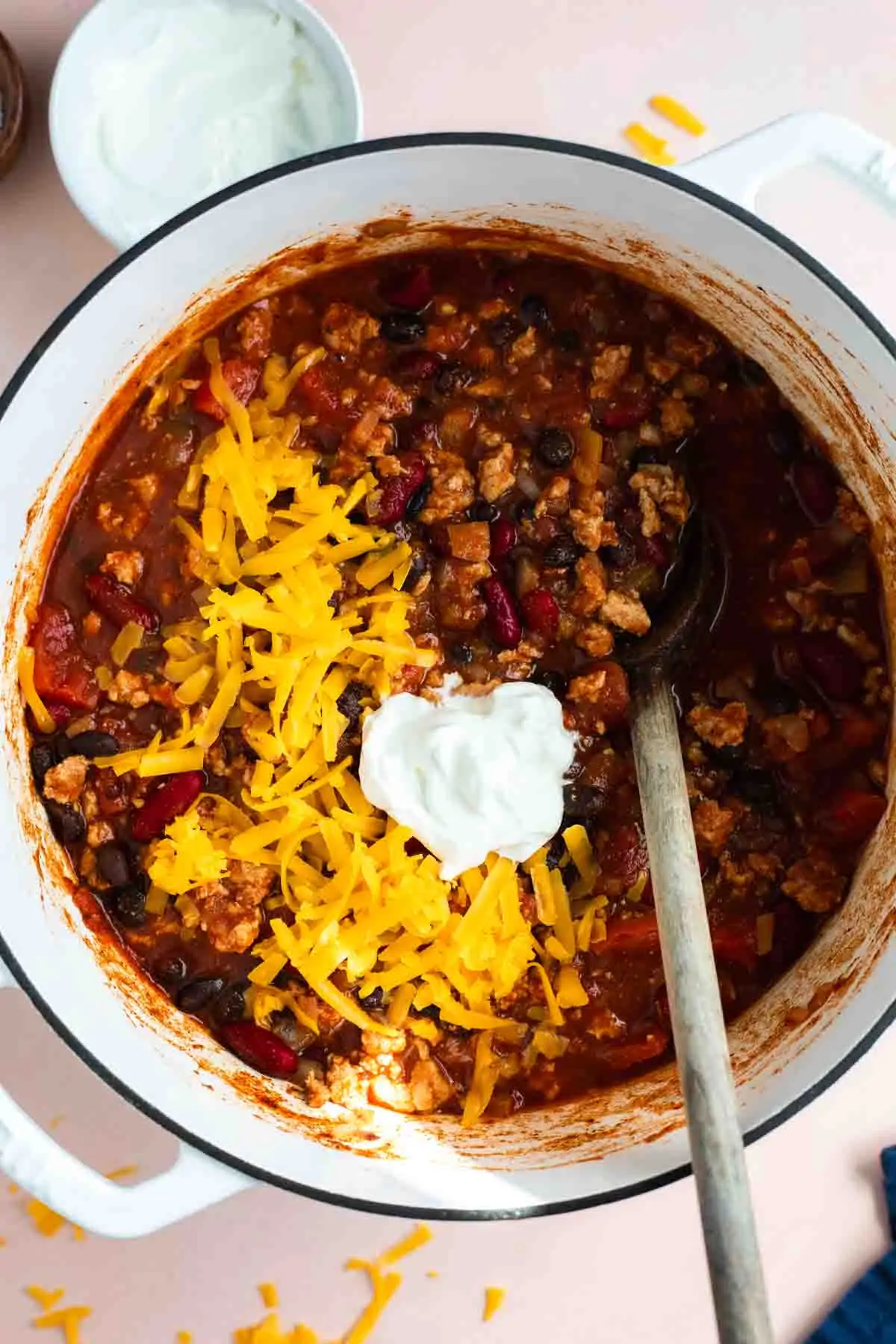 Pot filled with cooked turkey chili, topped with shredded cheese and sour cream.