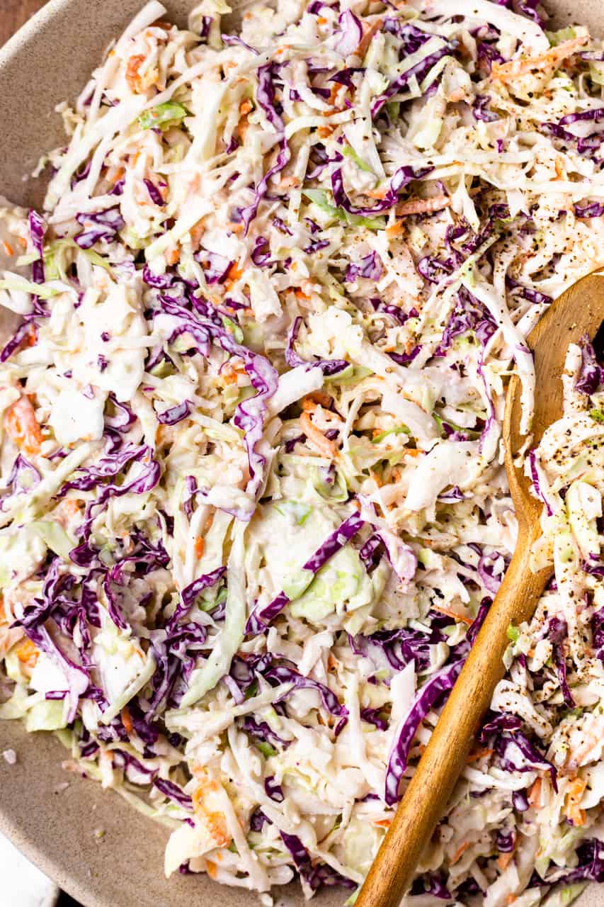 Up close view of mixed together coleslaw being served with wooden spoons.