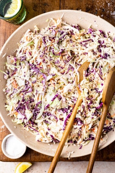 Bowl of coleslaw on a wood cutting board being served with wooden servers.