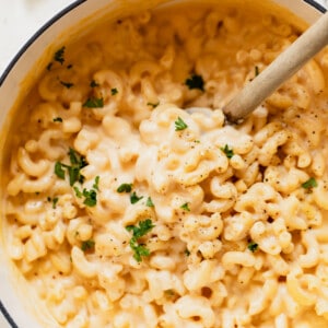 Dutch oven filled with creamy Mac and cheese with wooden spoon to serve.