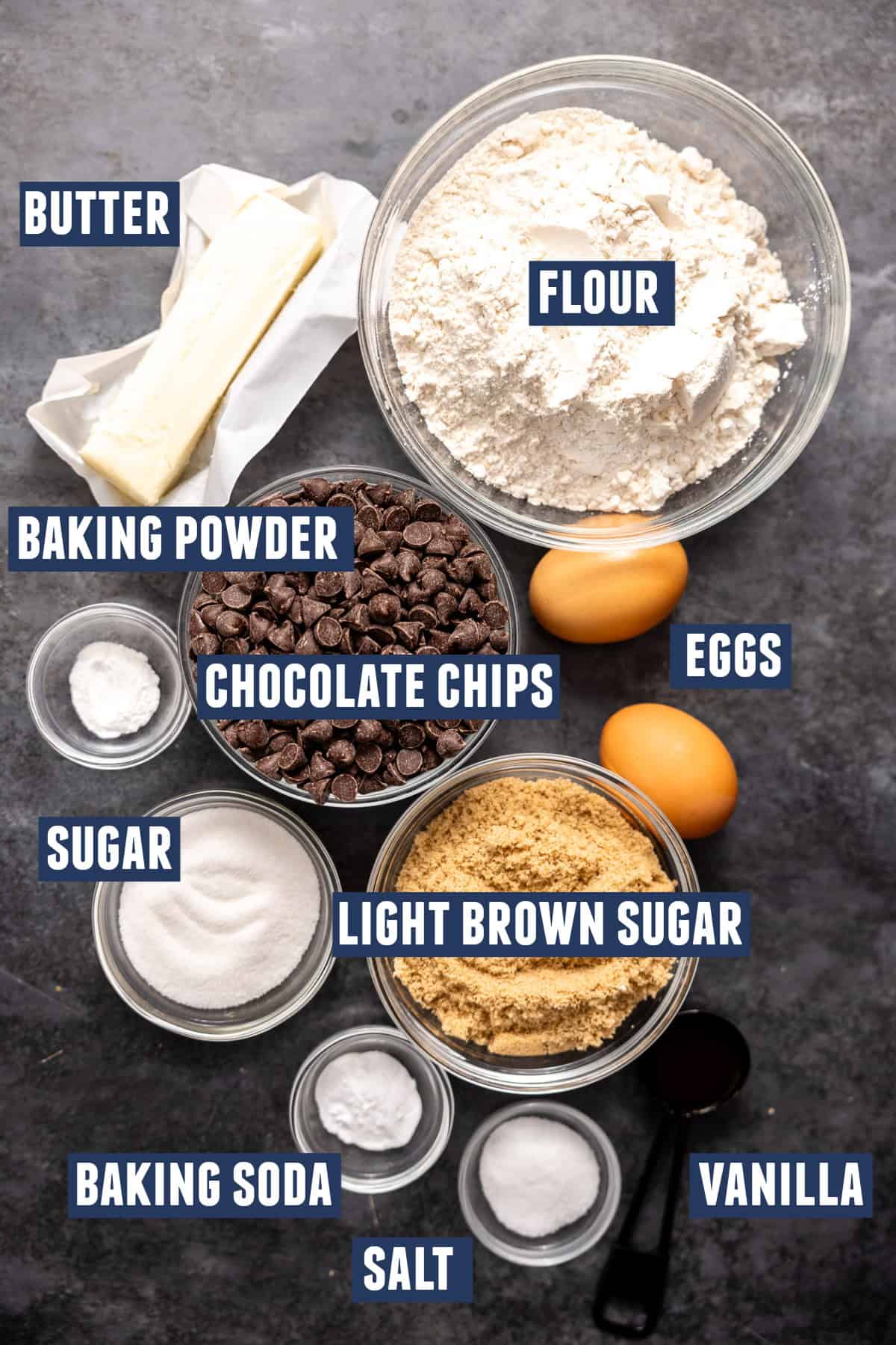 Ingredients needed to make thick chocolate chip cookies including: flour, light brown sugar, sugar, butter, eggs, salt, baking powder, baking soda, and vanilla. 