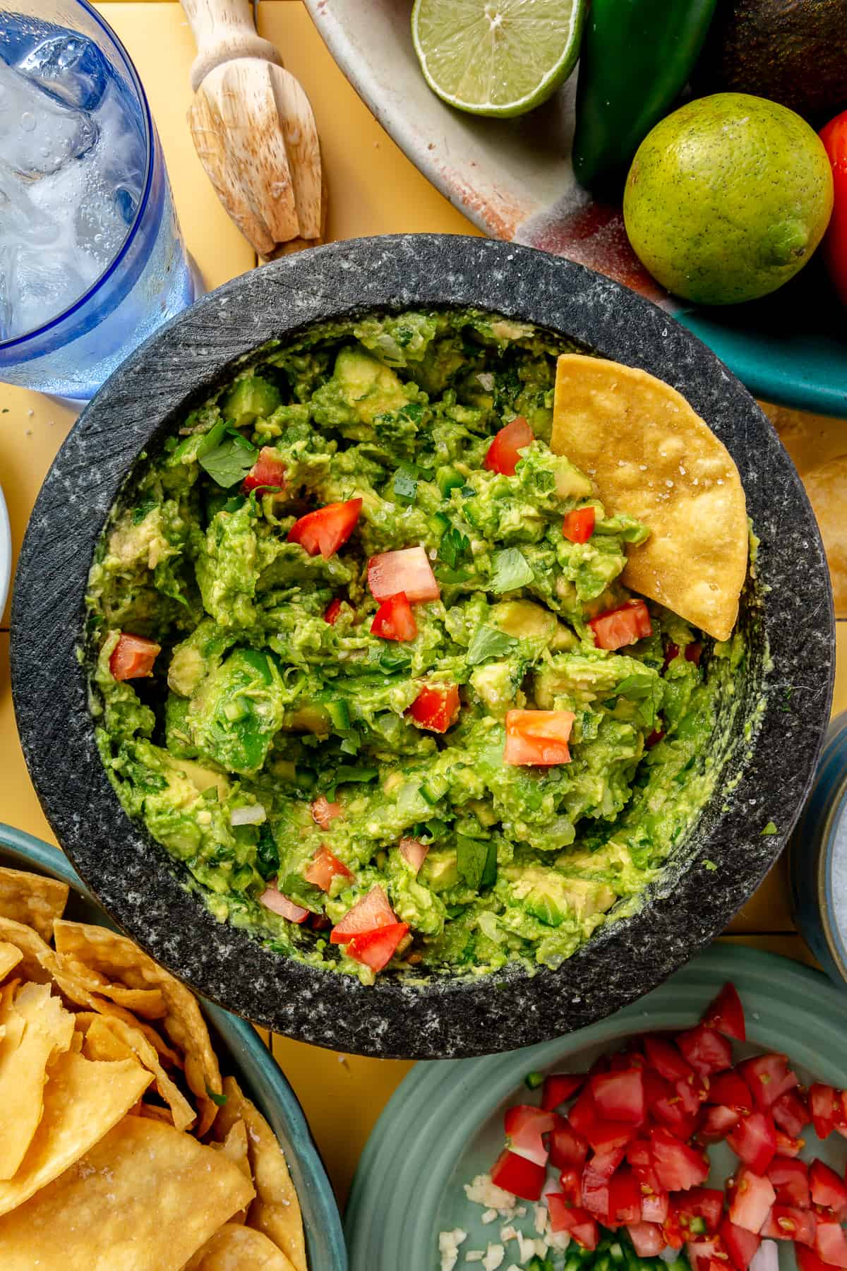 Molcajete filled with guacamole topped with tomatoes with tortilla chips dipped in it. 