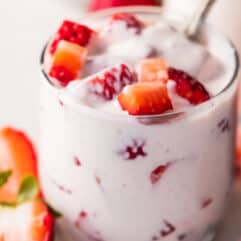 Glass filled with fresas con Crema, topped with diced strawberries and halved strawberries leaning against the cup.