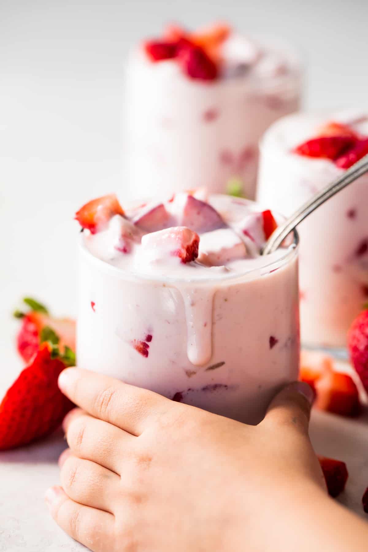 A cup filled with strawberries and cream being grabbed by a small Childs hand. 