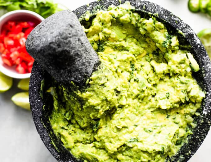 Freshly mashed guacamole with tomatoes, lime wedges, sliced jalapeno and cilantro on the side.
