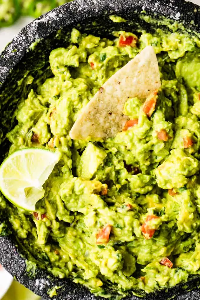 Molcajete filled with freshly made guacamole, with a tortilla chip sticking in it.