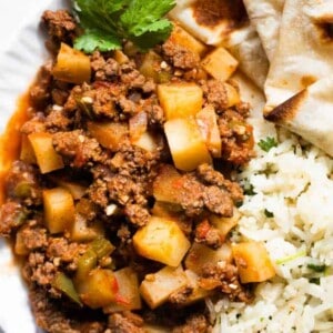 Overhead of picadillo on a white plate served with cilantro lime rice and flour tortillas.