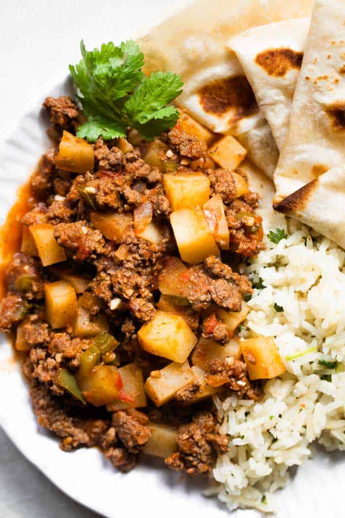 Overhead of picadillo on a white plate served with cilantro lime rice and flour tortillas.