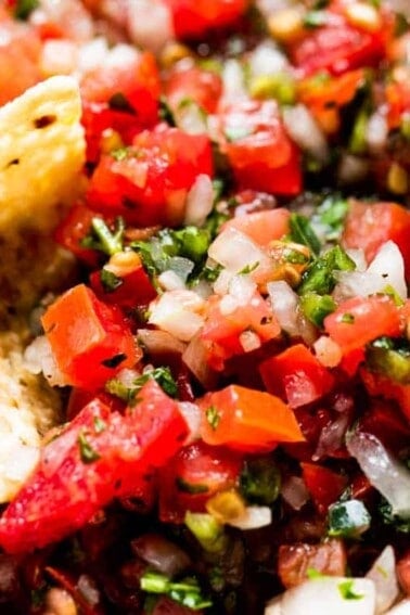 Chip dipping into a bowl filled with pico de gallo.