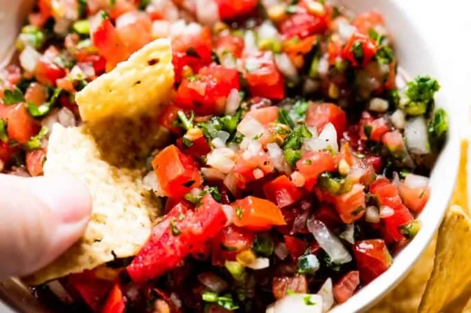 Chip dipping into a bowl filled with pico de gallo. 
