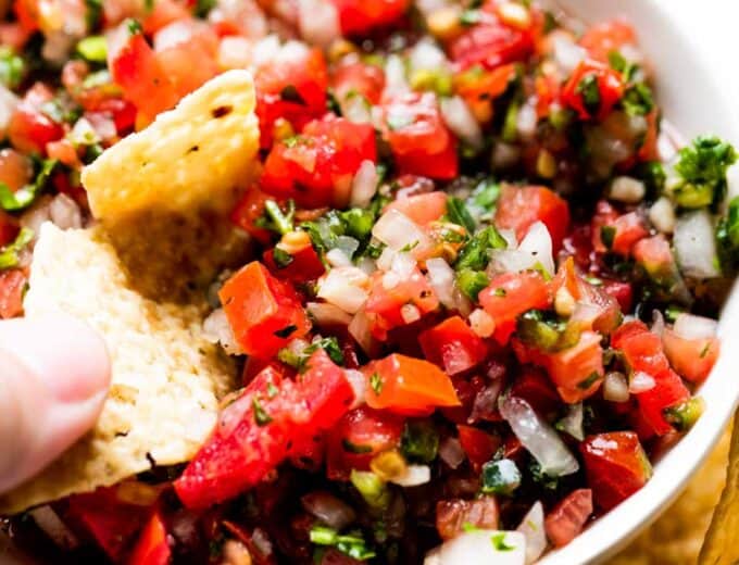 Chip dipping into a bowl filled with pico de gallo.