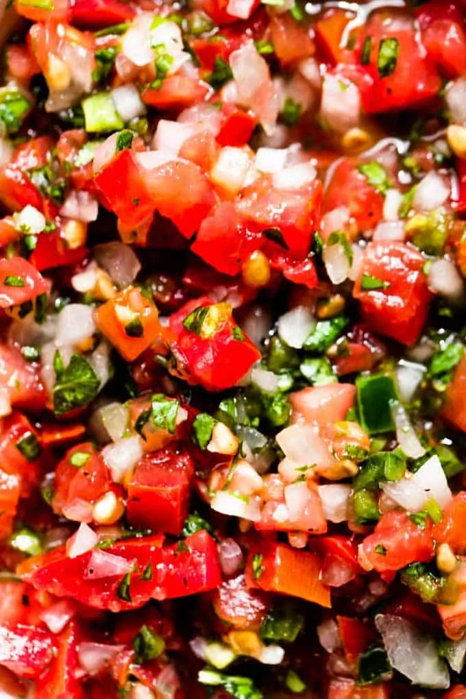 Up close view of pico de gall showing chunks of tomato, jalapeno and onion soaked in a lime juice. 