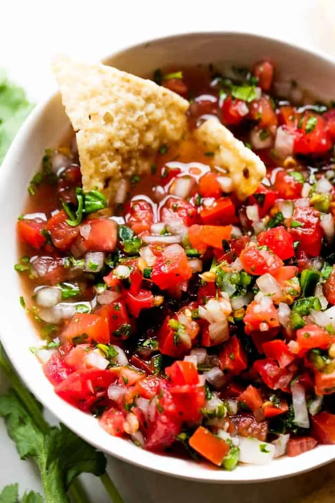 White bowl filled with pico de Gallo and a tortilla chip dipped in showing the juices.