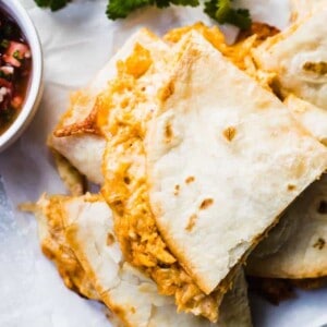 Stack of baked quesadillas with fresh cilantro, and a lime wedge on the side, plus a bowl of Pico de Gallo.