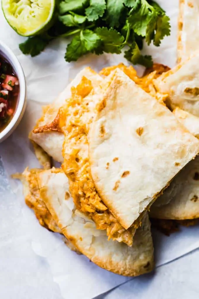 Stack of baked quesadillas with fresh cilantro, and a lime wedge on the side, plus a bowl of Pico de Gallo.