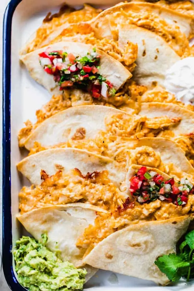 Tray filled with cut in half chicken quesadillas, garnished with a scoop of guacamole, sour cream and Pico de Gallo.