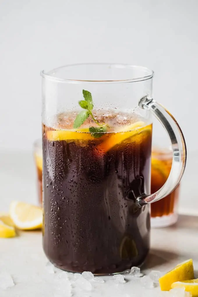 Pitcher of sweet tea, with condensation on the outside, ice chunks around it, and sliced lemon.