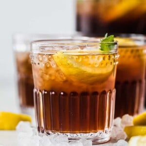 Cup of sweet tea in a glass topped with crushed ice, lemon wedge and a sprig of mint.