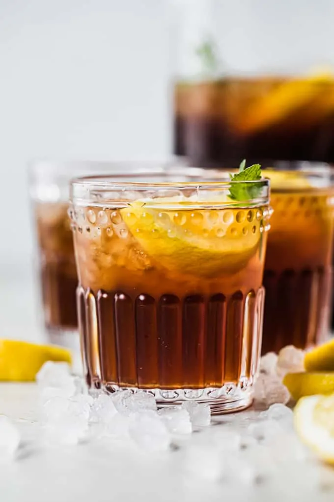 Cup of sweet tea in a glass topped with crushed ice, lemon wedge and a sprig of mint.