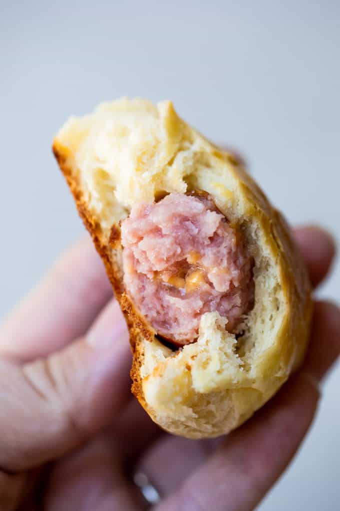 Image of a Sausage kolache bitten into showing fluffy breading around a cheese filled sausage.