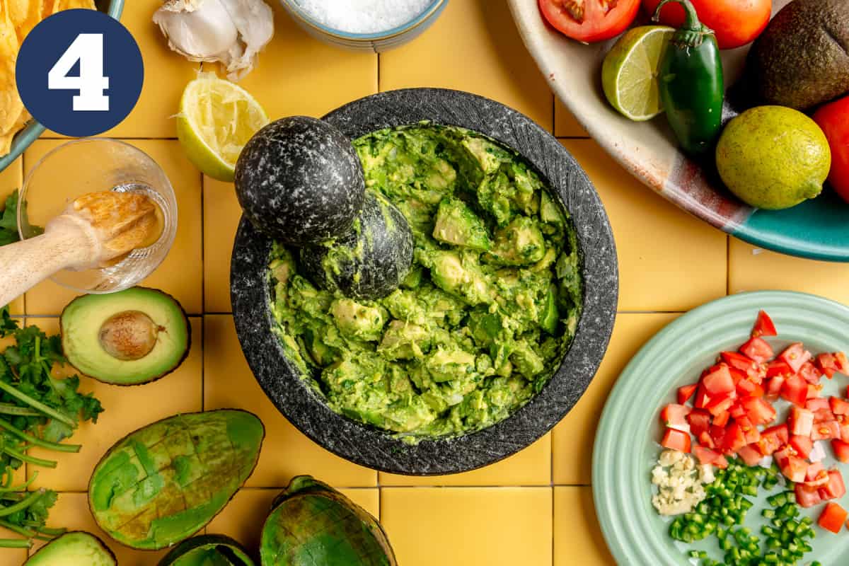 Avocado being mashed in a molcajete for tableside guacamole.