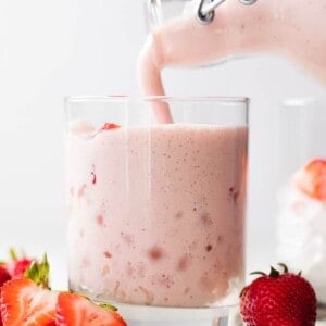 Fresh homemade agua de fresas with cream being poured into a cup with ice.