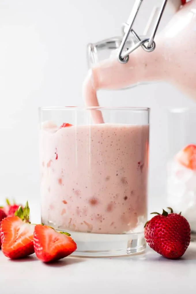 Fresh homemade agua de fresas with cream being poured into a cup with ice.